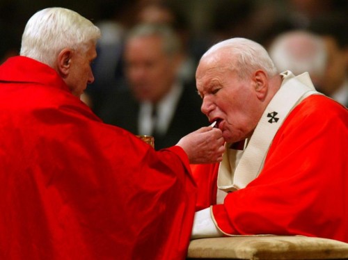 El cardenal Joseph Ratzinger -futuro papa Benedicto XVI- da la comunión en la boca al papa San Juan Pablo II.