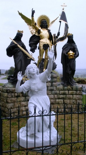 Aparición de San Miguel Arcángel y las Santas Catalina de Alejandría y Margarita de Antioquía a Juana de Arco. Conjunto escultórico conmemorativo en Domrémy-la-Pucelle (Francia).