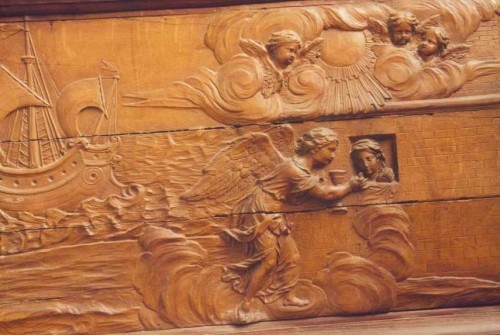 Santa Avia recibe de la comunión en prisión, de manos de un ángel. A la derecha, una de las naves de la compañía de Santa Úrsula. Relieve en madera. Colegiata de Nuestra Señora de Vernon, Canadá.